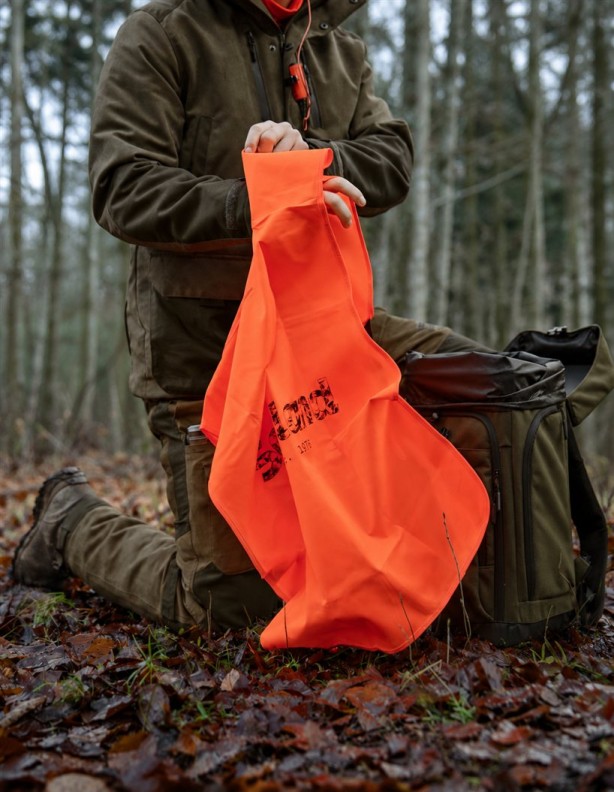 Myśliwy trzymający kamizelkę Seeland Safety Vest przy plecaku